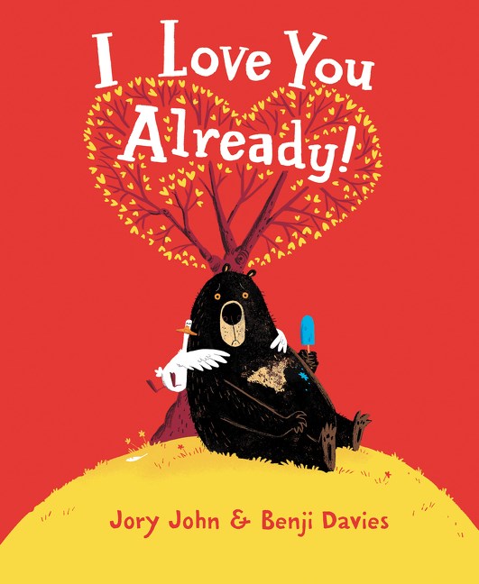 A black bear with a very mournful expression on his face sits beneath a tree whose leaves form a heart. A small duck wraps its wings around the bears arm, looking thrilled. Far more thrilled than the bear. Text: I Love You Already!
